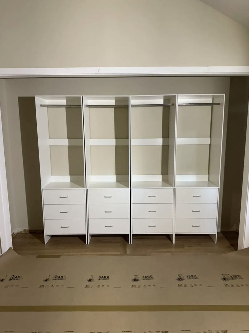 Four white closet towers with hanging rods, shelves and three drawers each, installed side by side in a closet opening
