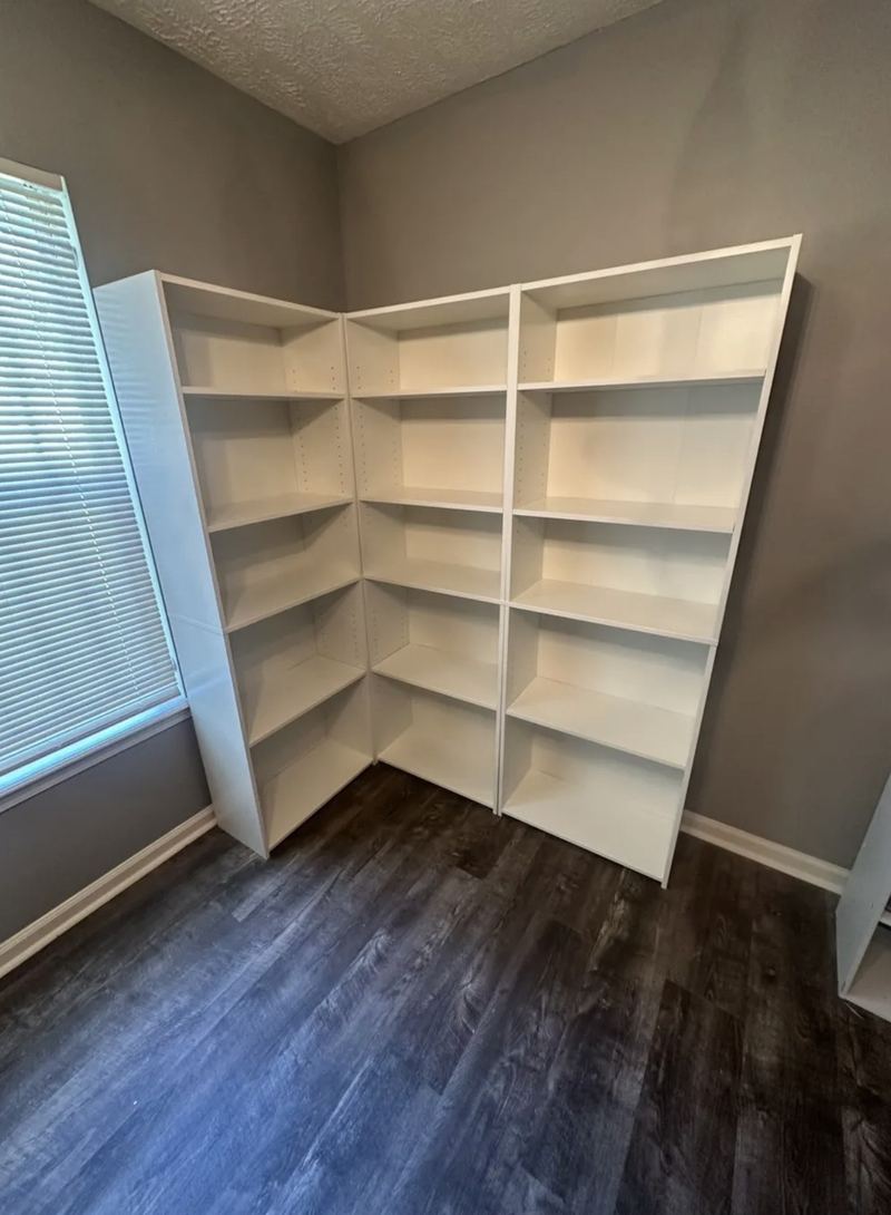 Three tall white bookcases arranged in an L around the corner of a room