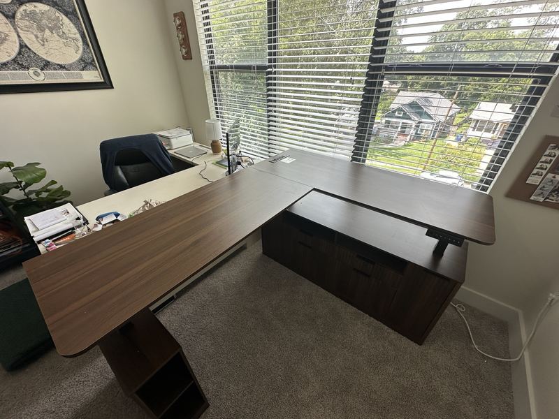 Large walnut L-shaped standing desk with a matching storage cabinet in a home office