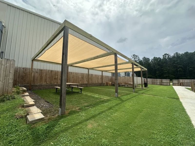 Large timber pergola with tan shade sails over picnic tables on a lawn