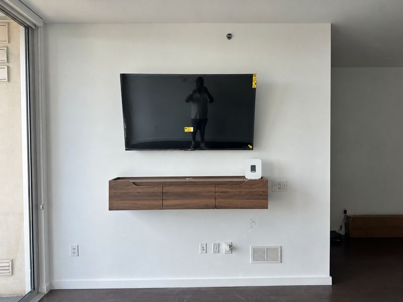 Flat-screen TV mounted level on a white living room wall above a floating walnut media console