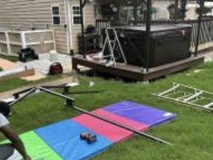 Gazebo frame pieces laid out on protective mats on the lawn beside a backyard deck