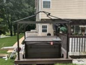 Gazebo frame standing over a hot tub on a backyard deck